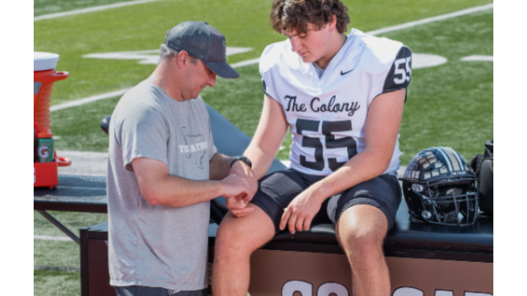 An athletic trainer assists a football player seated on a treatment table