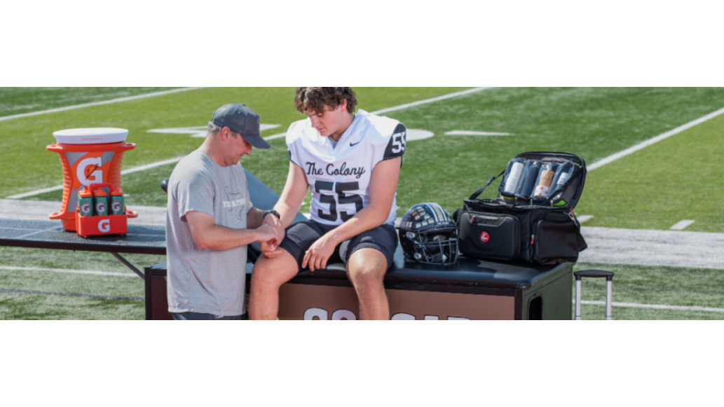 An athletic trainer assists a football player seated on a treatment table