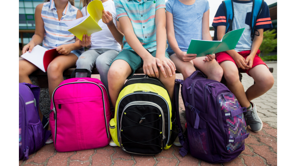 Children sit on a bench with their backpacks in front of them
