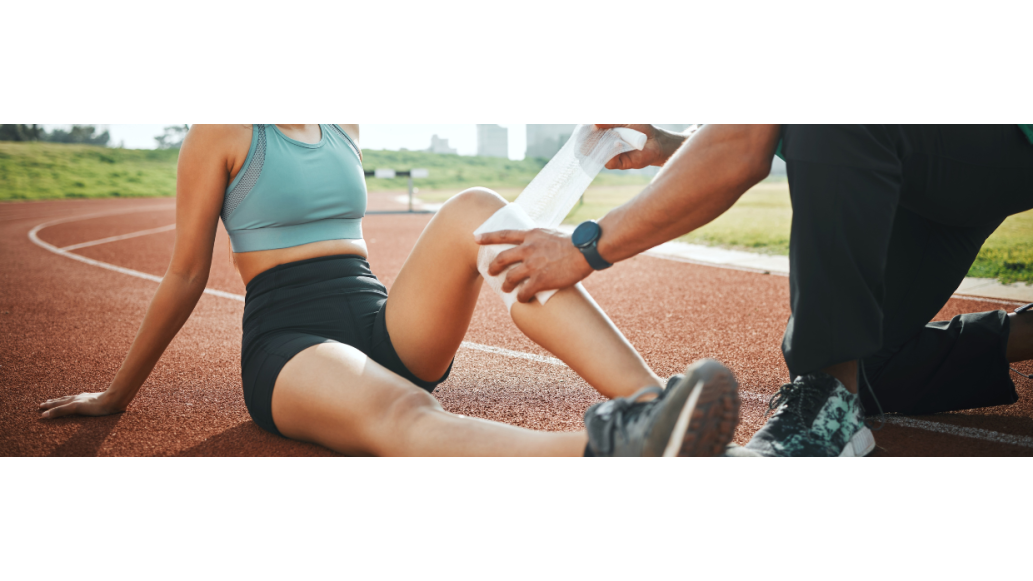 A female athlete is assisted with a knee wrap by an athletic trainer