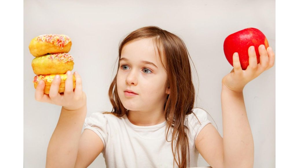 child holding a donut in one hand and an apple in the other